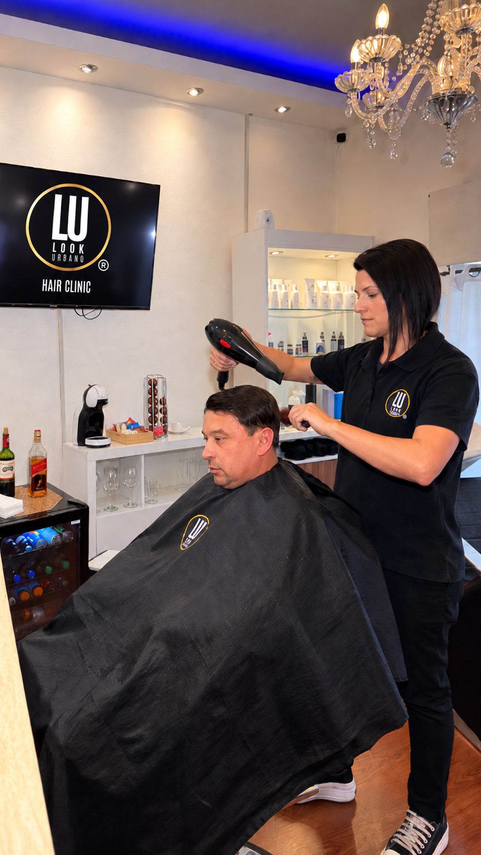Una técnica de Look Urbano peina a un cliente en el centro, frente al logo de Hair Clinic